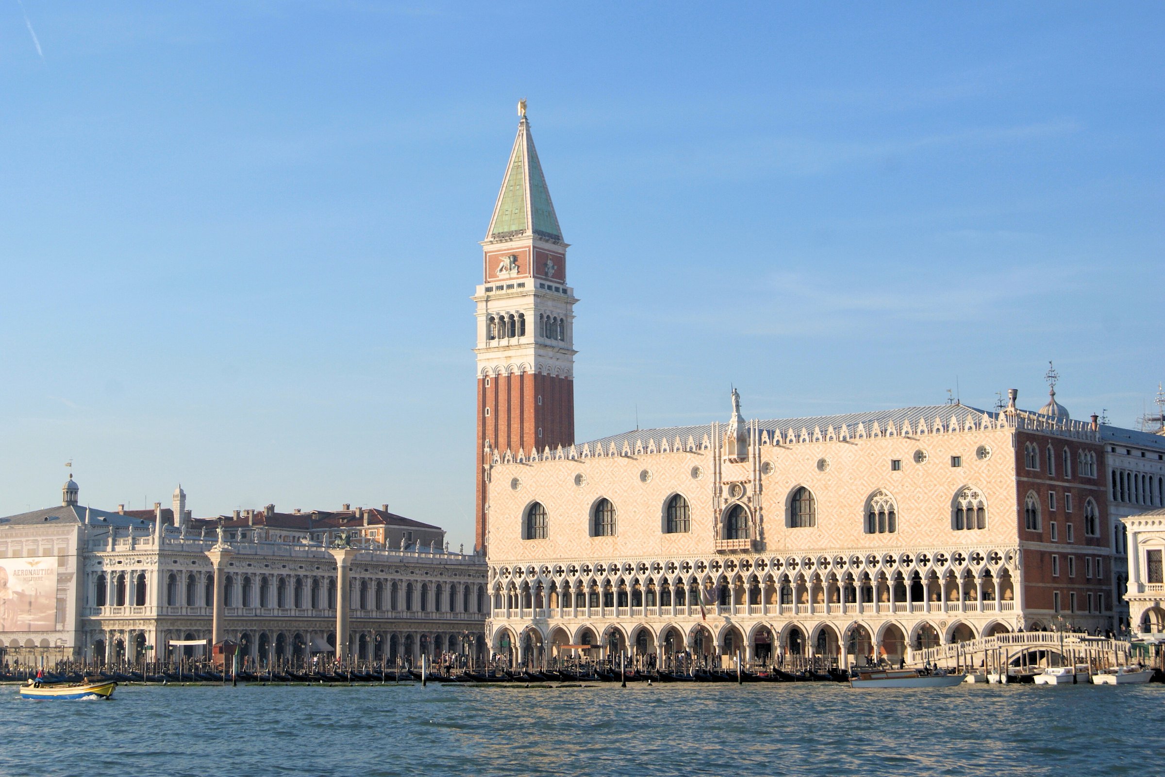 Panoramic view of the Doge's Palace and Campanile di San Marco from the water, showcasing Venice’s iconic architecture against a clear blue sky.