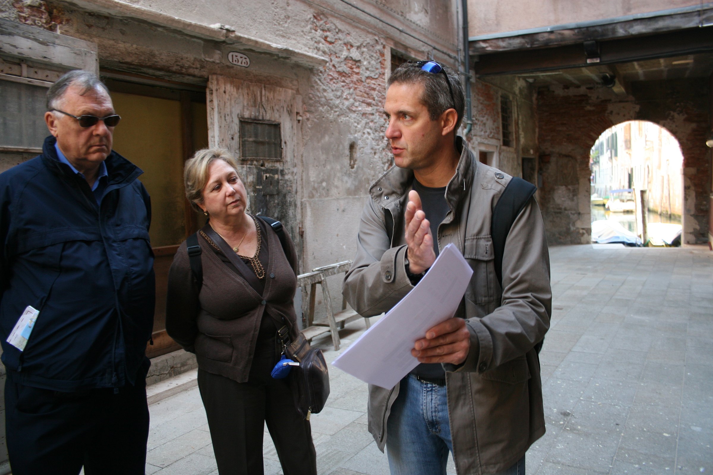 A guide explains Cannaregio’s history to two visitors in a quiet alleyway.