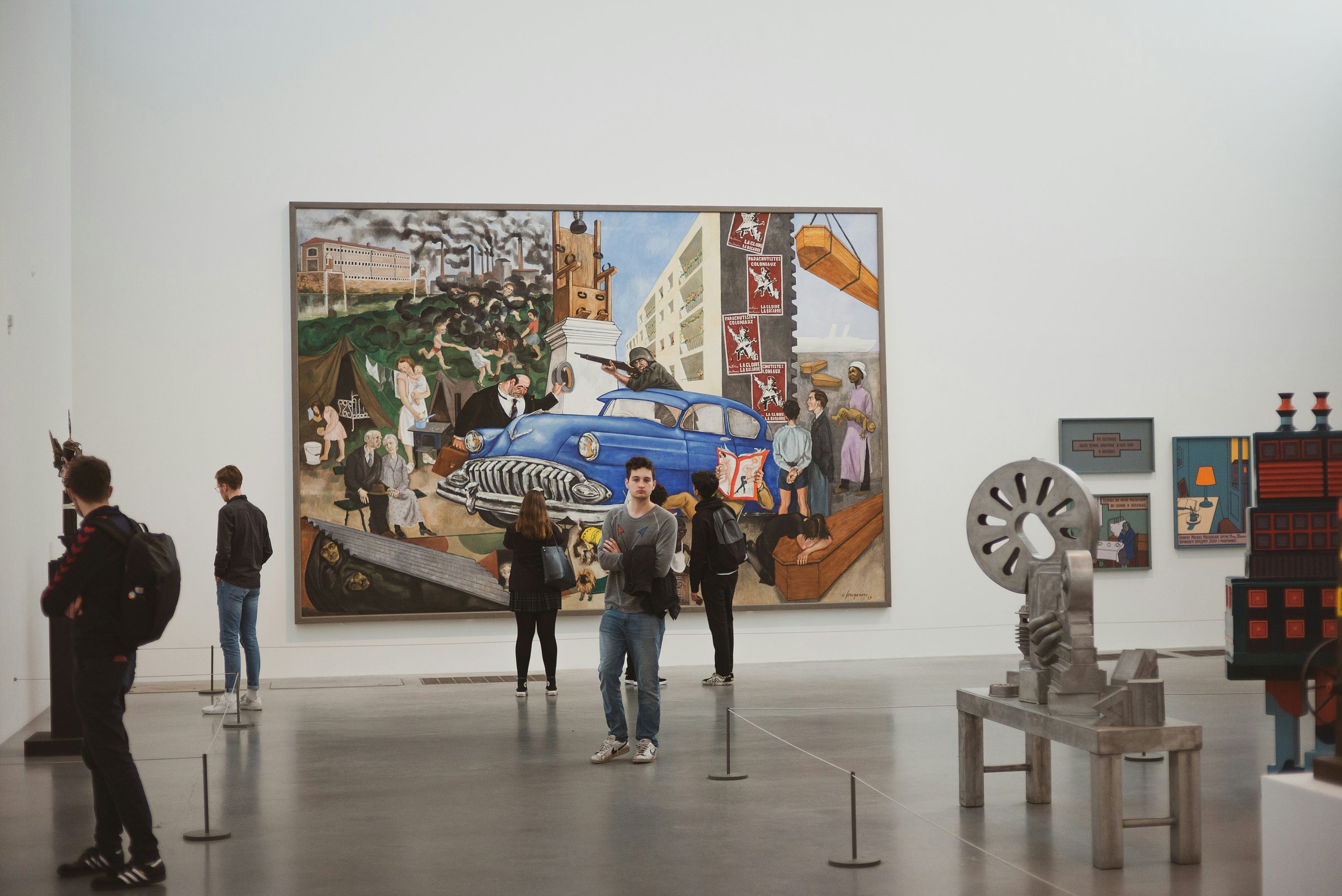 Visitors viewing a large industrial-themed painting and modern sculptures inside a spacious gallery at Tate Modern.